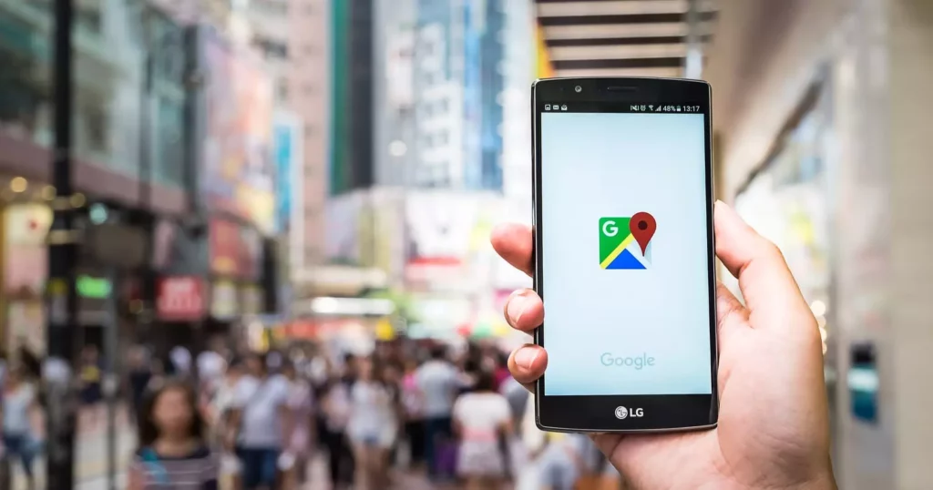 A person holds an LG smartphone displaying the Google Maps app with a city street and a crowd of people blurred in the background, highlighting the importance of Local SEO in optimizing your Google Business Profile. - Ketamine